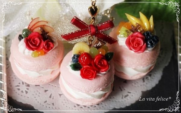 ピンクのマカロンに赤いバラと色鮮やかなフルーツを飾ったフェイクスイーツチャーム3点。レースペーパーの上に並べられた華やかな作品。